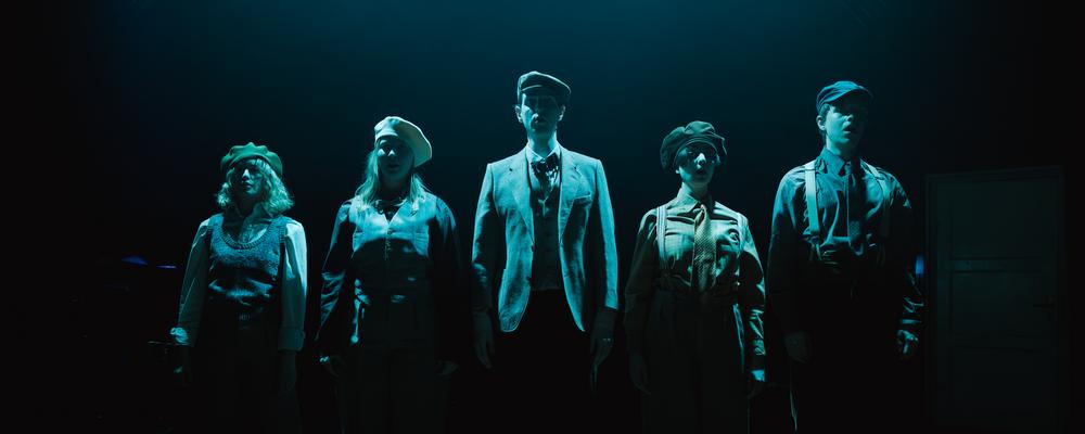 Five opera students standing in a row on stage under dark stage lighting