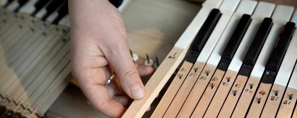 En hand lägger en tangent i mekaniken av en klaviatur