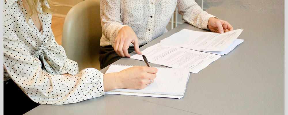 Två tjänstepersoner sitter vid mötesbord och pratar om dokument