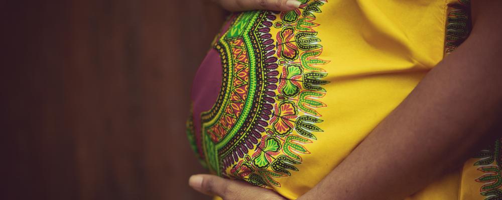 kvinna i färgglad klänning håller om sin gravida mage