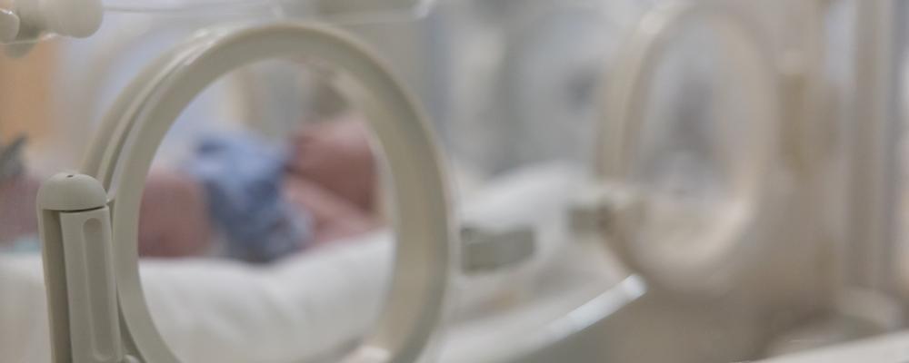 Prematurt barn i kuvös, sett genom plastfönster