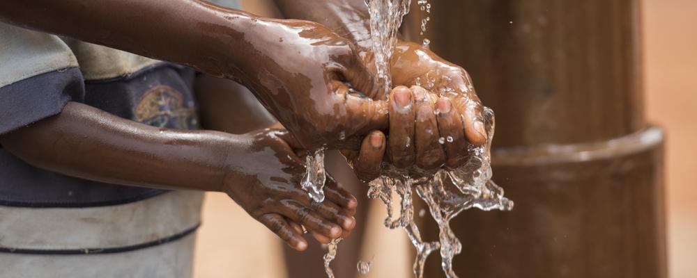 Child washing hands under water from pump