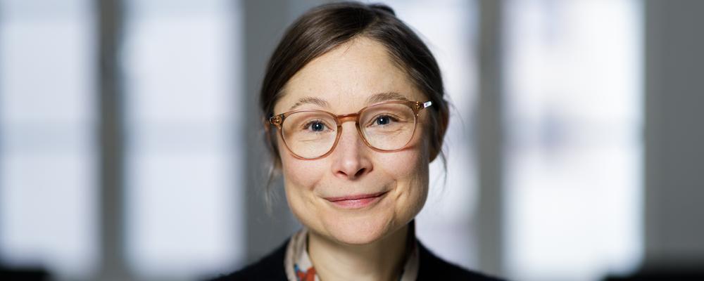 En kvinna sitter i ett rum där fönster släpper in ljus bakom henne