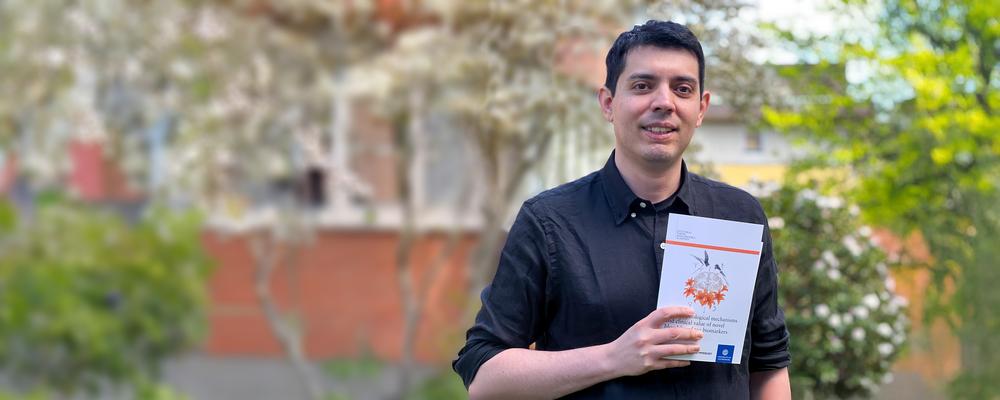 Man standing outdoors holding up his thesis toward the camera