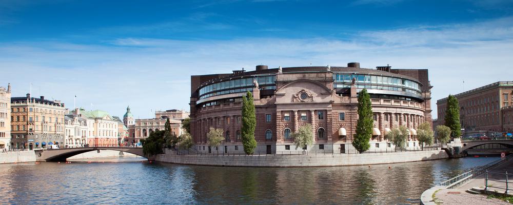 Riksdagshuset i Stockholm, sett från andra sidan vattnet under en klarblå himmel.