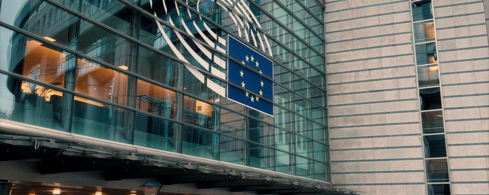 Europaparlamentets byggnad i Bryssel med EU-flaggor och medlemsländernas flaggor framför moderna glas- och stålbyggnader under klar himmel.
