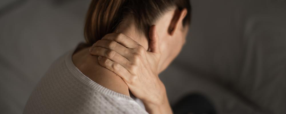 Kvinna sedd bakifrån gnider sin nacke
