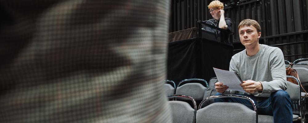 One person with sheet music in their hands, another at a mixing console