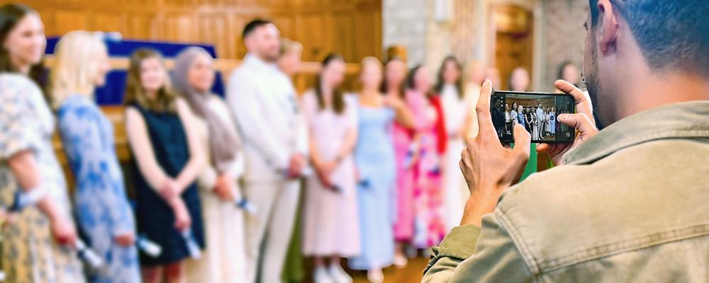 Person fotograferar examensstudenter som poserar för gruppbild i aula.