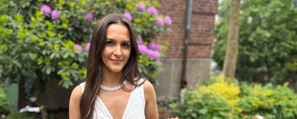 student vanesa står finklädd i trädgård på examensdagen 