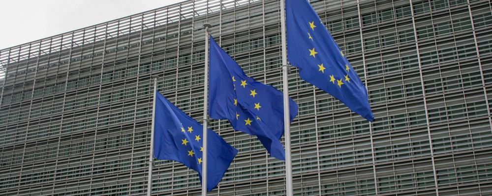 Three European flags in front of a building that can be interpreted as a fence