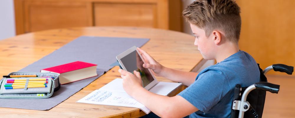 Boy in wheelchair doing homework and using tablet pc.