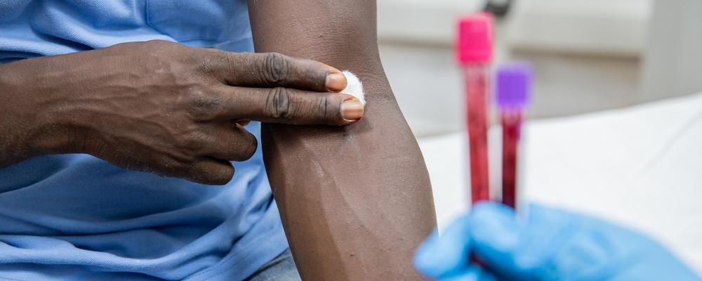 Older Black adult after a blood draw, with blood sample tubes in foreground.