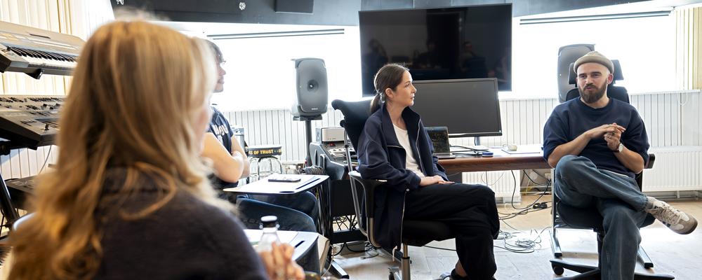 Four people are sitting in a recording studio and having a discussion.
