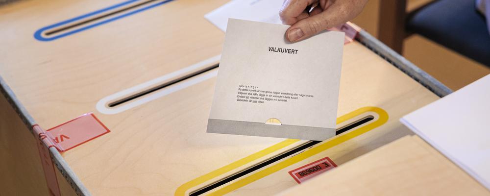 En röstmottagare stoppar ett valkuvert i en valurna.