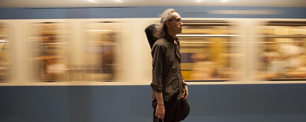 en person med en elbas, ett tunnelbanetåg åker förbi i bakgrunden