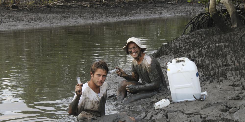 Issac Santos och student Justin Gleeson sitting i a swamp all muddy 