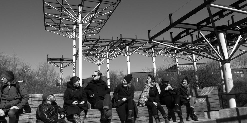 En grupp personer sitter framför ett konstverk med metallpelare