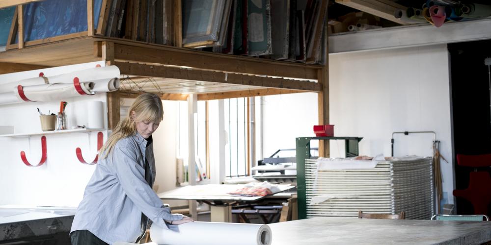 Helena i en av sina ateljéer i huset i Bohuslän i bakgrunden syns ramar för textiltryck