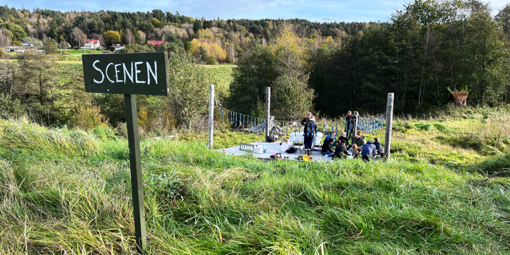 En grässlänt och en skylt med ordet "Scenen"