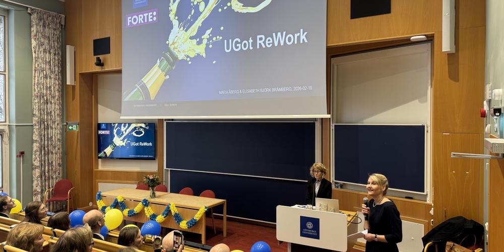 Två personer står längst fram i en hörsal och talar till publiken under invigningen av UGot ReWork. En presentationsbild med cen