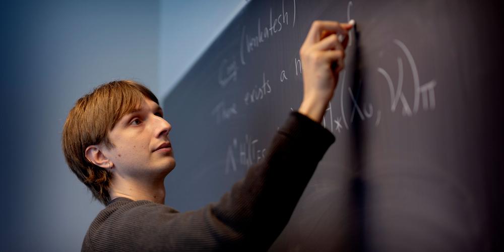 Ung man skriver matematiska formler på en tavla