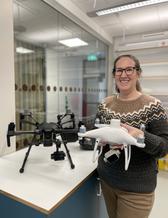 En kvinna står i ett lab med och håller i en drönare. 