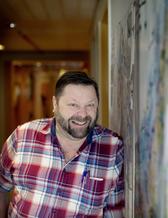 A man in chequered shirt leaning against a wall