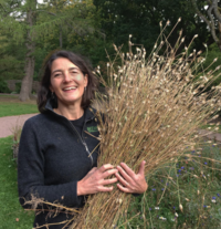 A smiling Helen Ekvall standing holding a bunch of dried grass 