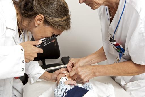 två personer i vita rockar undersöker ögon på ett spädbarn