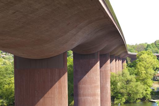 Bilden visar en rosafärgad bro i betong snett underifrån med kraftiga runda bropelare. 