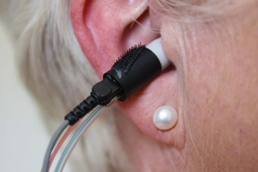 A person has an earplug with tiny cables going into it during a phonometry.