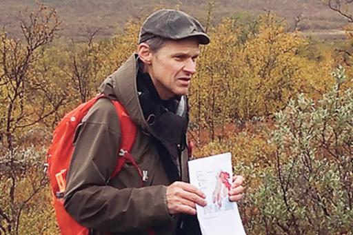 Mats Olvmo står på en myr, visar karta, berg syns.