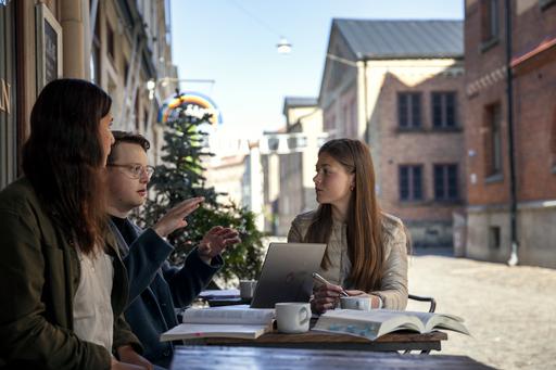 Tre studenter sitter vid ett cafébord utomhus i Haga och pluggar.