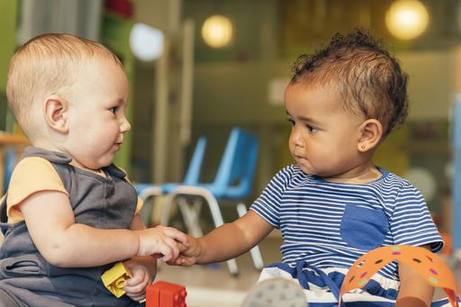 Två spädbarn tittar varandra i ögonen och håller varandra i handen.