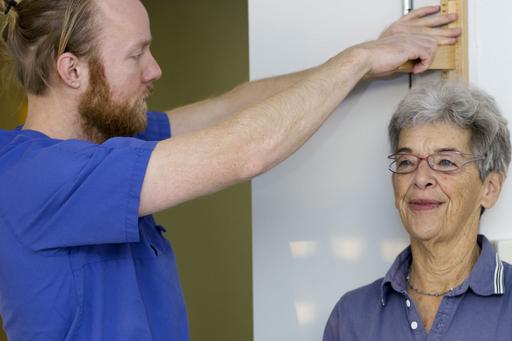 Sjuksköterska mäter kvinnas längd mot en vägg