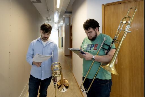 Två personer med tromboner står i en korridor och läser i var sitt papper