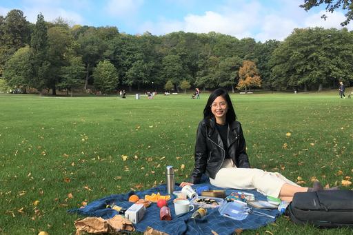 Student Hanh sitting on a blanket and having a picnic in a park surrounded by trees