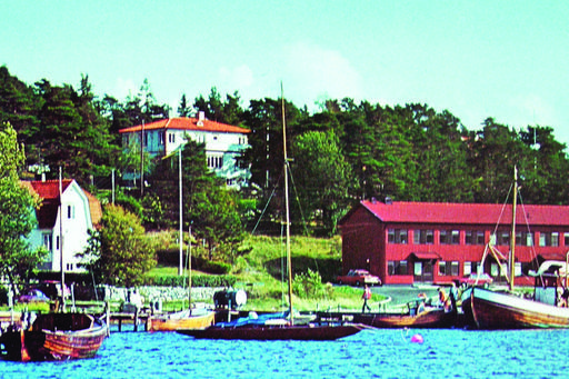 Röda byggnader vid vattnet. Båtar ligger förtöjda vid bryggan.