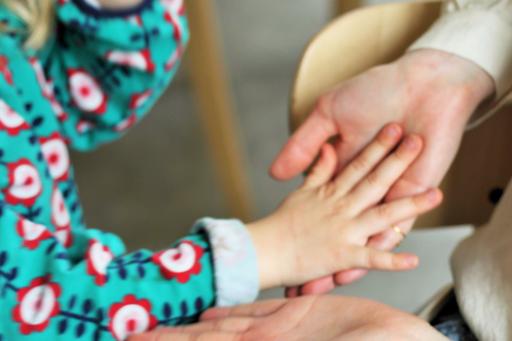 The image shows the hands of an adult woman holding the hands of a small child.