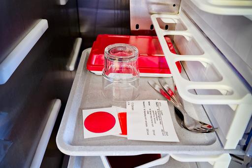 rostfri vagn med flera brickor med mat fokus på översta med glas, låda och bestick.