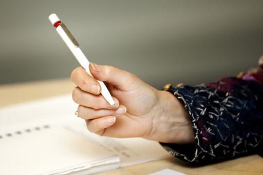 Hand som håller i penna samt skrivpapper på bord