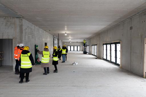 A large building under construction. A few people in high-visibility clothing are walking around.