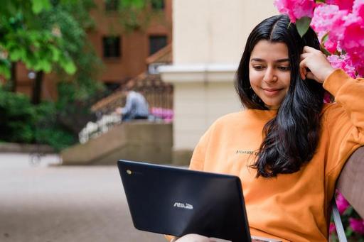 kvinna om sitter på bänk och kollar i sin dator