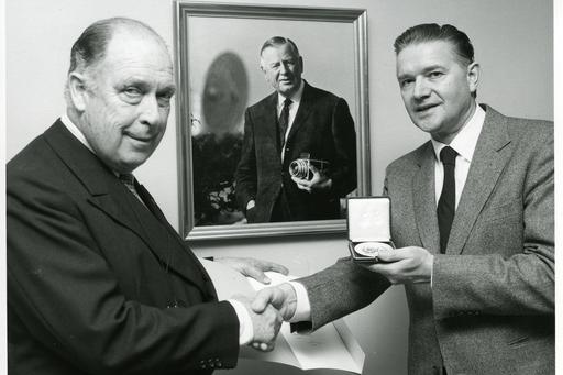 Two men shaking hand, one holding a medal.