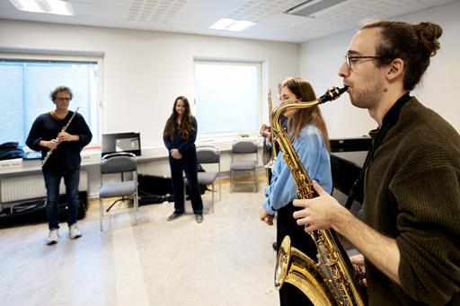 Saxofonist spelar och fyra andra musiker lyssnar.