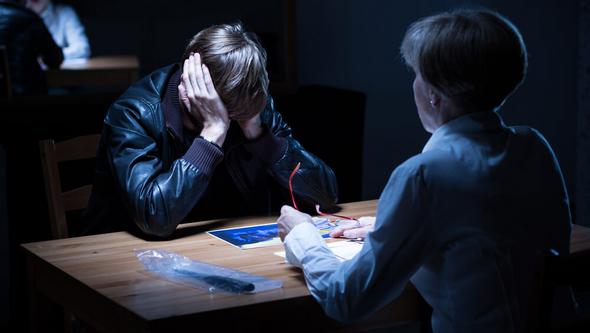 Young person sitting being interrogated in dark room