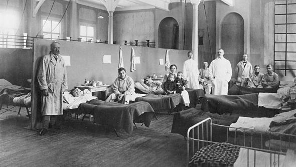 Svartvitt foto från 1918 med patienter liggande i sängar och läkare stående bredvid