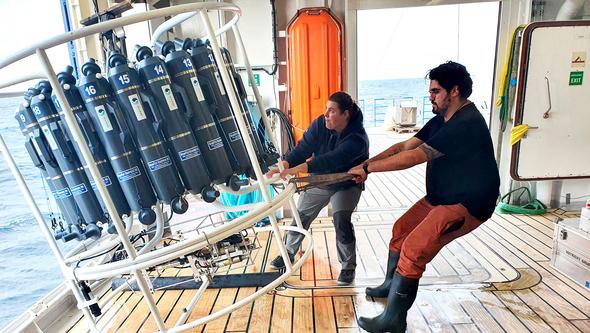 Två personer på ett fartyg håller i ett mätinstrument. 