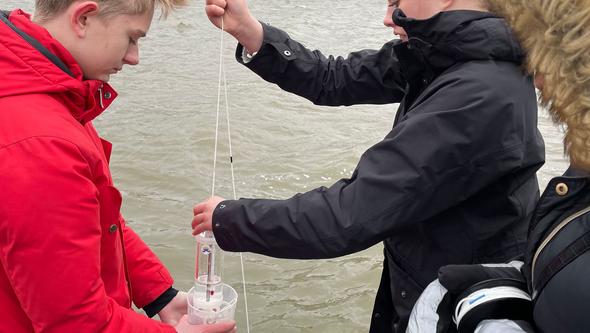Två barn står vid vattnet och håller i ett mätinstrument.